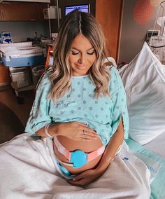 a pregnant woman sitting in a hospital bed with her stomach wrapped around an object that is shaped like a heart