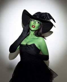 a woman dressed in green and black with a hat on top of her head, posing for the camera