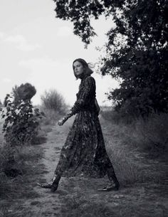 a woman walking down a dirt road next to trees