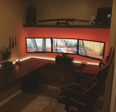 a desk with two monitors on it in front of a red wall and some lights