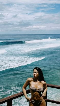 a woman standing on top of a wooden railing next to the ocean with waves in the background