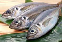 three fish sitting on top of a green leaf covered table next to a wooden surface