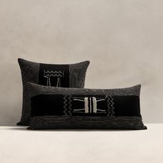 two black pillows sitting on top of a white table next to each other and one has a decorative design on it