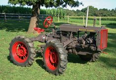 an old farmall tractor parked on the grass in front of a tree and fence