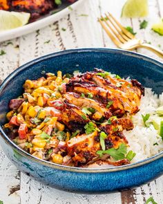 a blue bowl filled with rice and chicken next to a plate full of corn on the cob