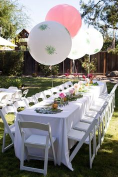 a long table with white chairs and balloons