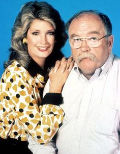 an older man and woman posing for a photo together in front of a blue background