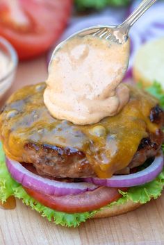 a hamburger with lettuce, tomato and cheese on it being held by a fork