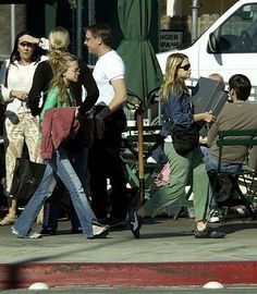 people are walking down the street in front of an umbrella and some tables with chairs