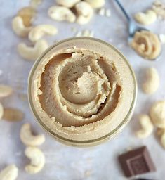 a jar filled with peanut butter next to cashews on a white counter top