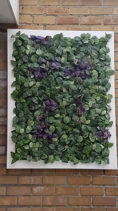 a square white frame with purple and green leaves on the side of a brick wall