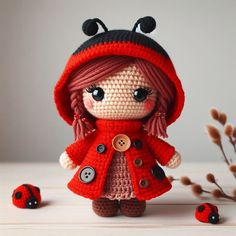 a crocheted doll wearing a red coat and hat next to some ladybugs