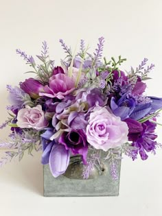 purple flowers and greenery are arranged in a square metal container on a white background