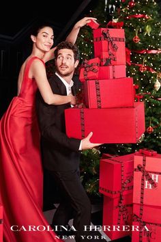 a man and woman are posing with presents in front of a christmas tree