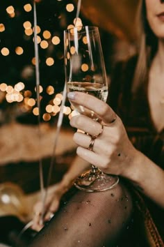 a woman holding a wine glass in front of a christmas tree with lights on it