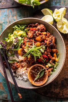 a bowl filled with rice and meat next to chopsticks on a wooden table