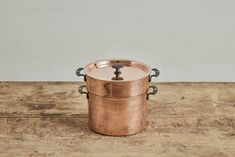 a large copper pot sitting on top of a wooden table next to a white wall