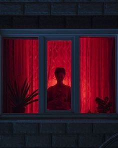 a woman standing in front of a window with red light coming through the windows and curtains