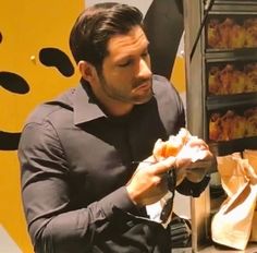 a man eating food from a paper bag in front of a display case with pastries