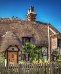 an old thatched cottage with a wooden fence and green plants on the front yard