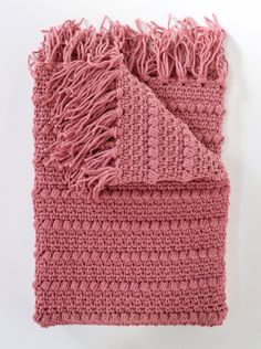 a pink crocheted blanket with fringes on it