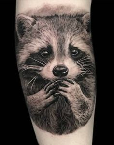 a raccoon tattoo on the leg with its hands clasped to it's face