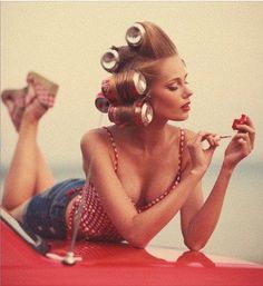 a woman sitting on top of a red car with lots of hair blowing in the wind