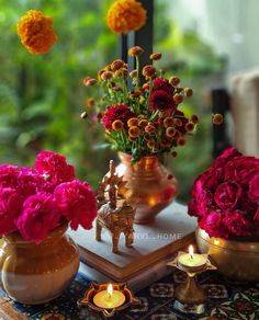 vases with flowers and candles on a table in front of a window, next to an open book