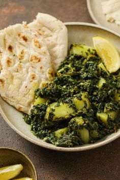 a bowl filled with food next to two slices of lemon wedges and a pita bread