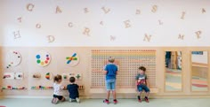 three children are standing in front of a wall with letters and numbers on the walls