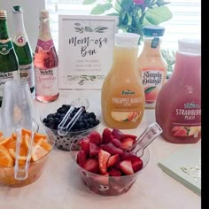 fruit and juices are on the table next to each other, including oranges, strawberries, blueberries, raspberries, and peaches