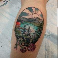 a person with a tattoo on their leg that has a lake and mountains in the background