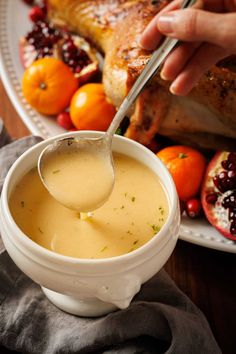 a person spooning some food out of a white bowl with oranges and cranberries on the side