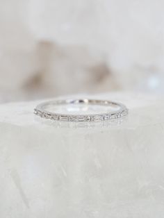 a white gold wedding band with round diamonds on top of a marble slabd surface