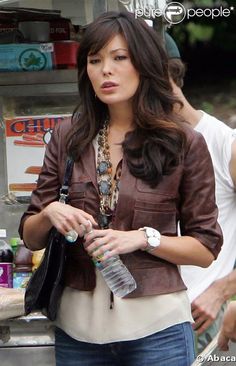 a woman standing in front of a food stand holding a bottle and looking at the camera