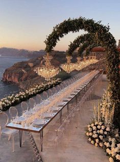 a long table set up with white flowers and candles for an outdoor wedding reception overlooking the ocean