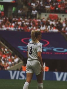 a female soccer player is standing on the field in front of an arena full of people