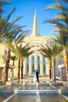 a bride and groom standing in front of a church with palm trees on the grounds