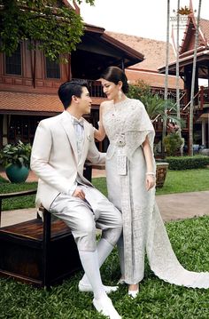 a man and woman sitting on a bench in front of a building with green grass