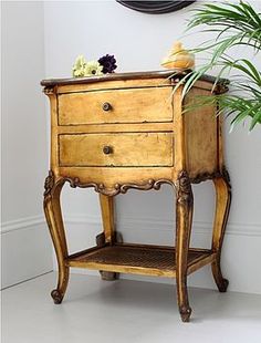 a small wooden table with two drawers next to a potted plant