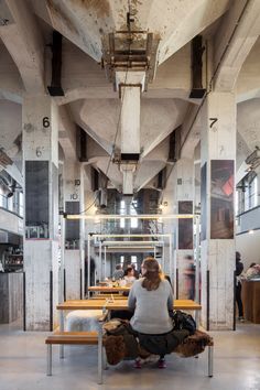 a woman sitting on a bench in an industrial building with exposed ceilings and wooden benches