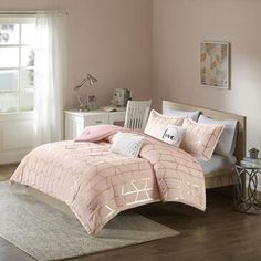 a bed with pink comforter and pillows on top of it in a room next to a window