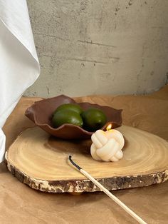 a candle and some fruit are on a wooden slice with a stick in front of it