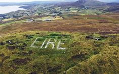 an aerial view of the word live written in grass on top of a hill with water and mountains behind it