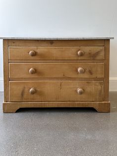 a wooden dresser with three drawers and marble top