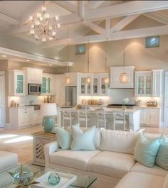 a living room filled with furniture and a chandelier hanging from the ceiling in front of a kitchen