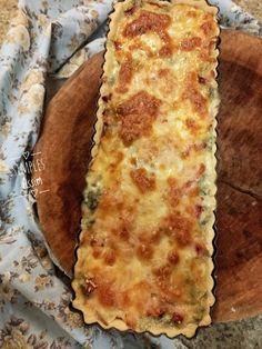 a cheesy quiche sitting on top of a wooden cutting board next to a blue and white cloth