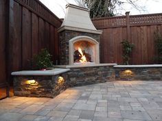 an outdoor fireplace in the middle of a brick patio with lights on and around it