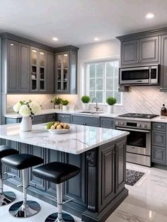 a large kitchen with gray cabinets and marble counter tops, two stools in front of the island