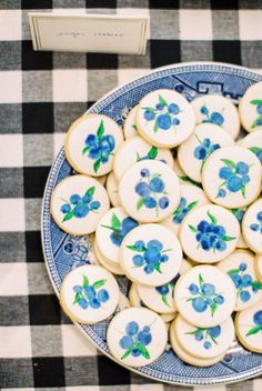 a plate full of decorated cookies on a checkered tablecloth with a box of cookies in the background